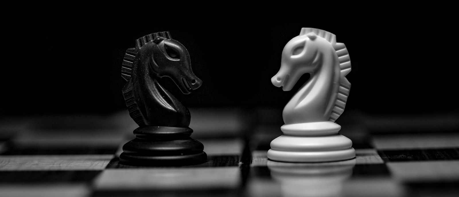 A black and a white chess knight facing each other on a board