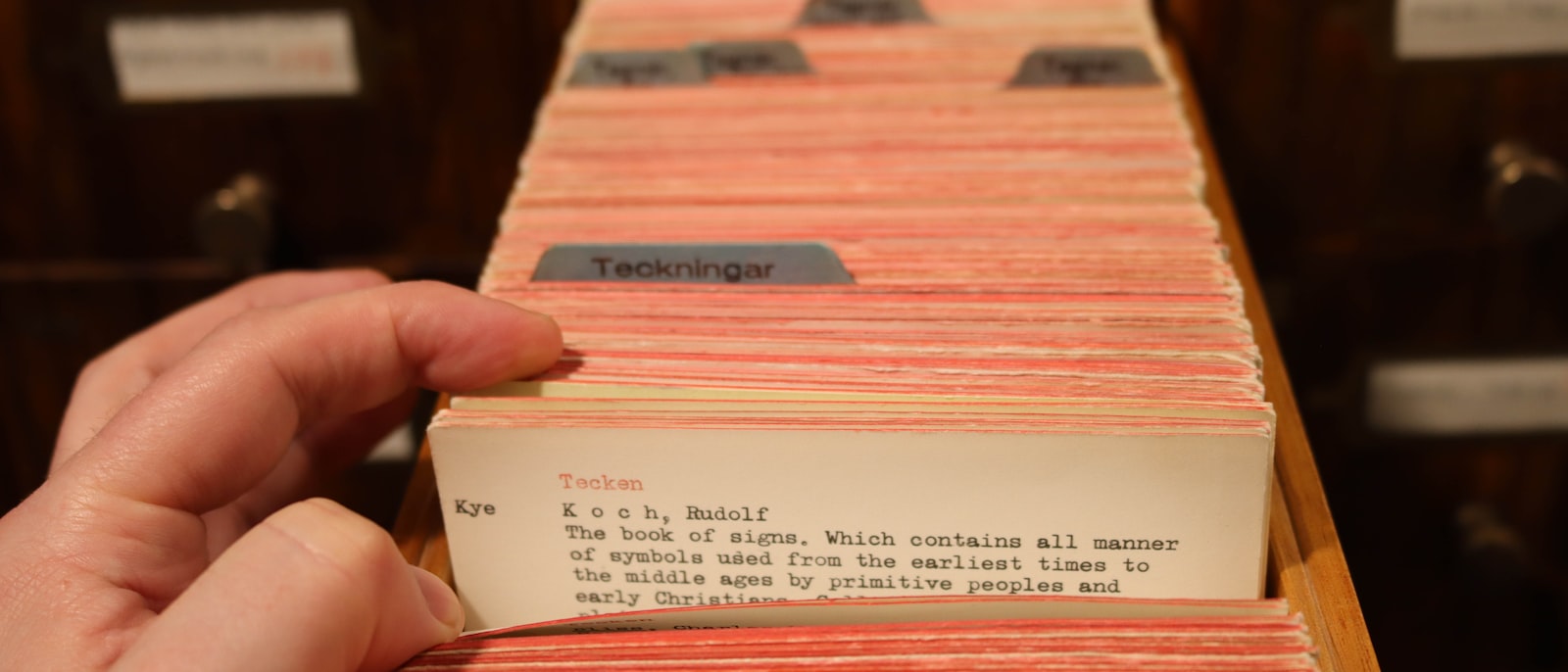 A hand pulls a card from the library's card catalog